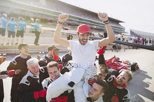 Equipe de Fórmula 1 carregando motorista nos ombros, celebrando a vitória na pista de esportes — Fotografia de Stock