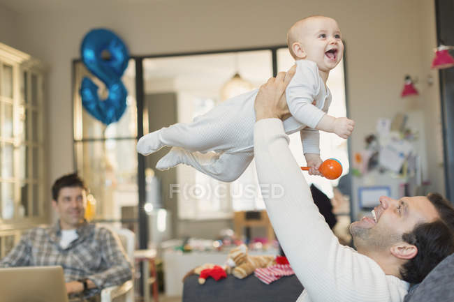 Male gay parents lifting and playing with baby son in living room — Stock Photo