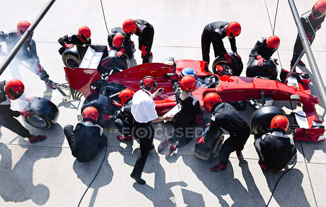 Manager with stopwatch timing pit crew replacing tires on formula one race car in pit lane — Stock Photo