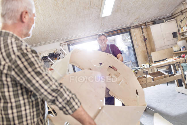 Carpinteiros masculinos movendo casca de barco de madeira na oficina — Fotografia de Stock