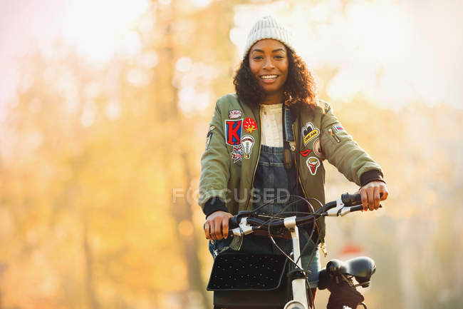 Portrait smiling young woman with bicycle in front of autumn trees — Stock Photo