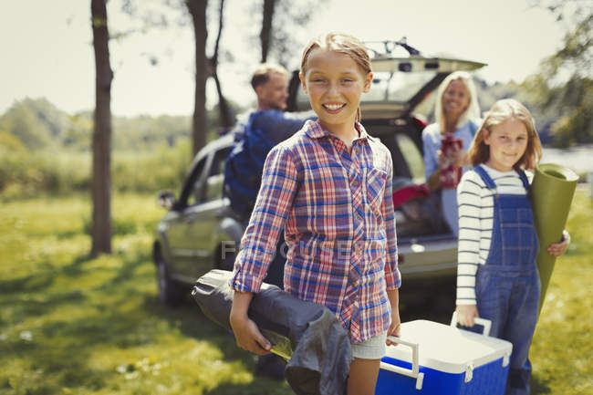 Портрет улыбающейся семьи, выгружающей оборудование для кемпинга из автомобиля — стоковое фото