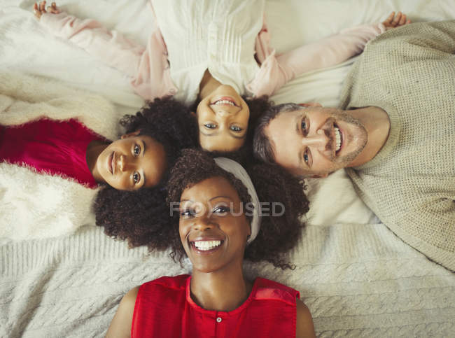 Overhead portrait smiling multi-ethnic young family laying on bed — Stock Photo