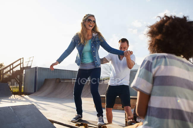 Boyfriend helping girlfriend on skateboard in sunny skate park — Stock Photo