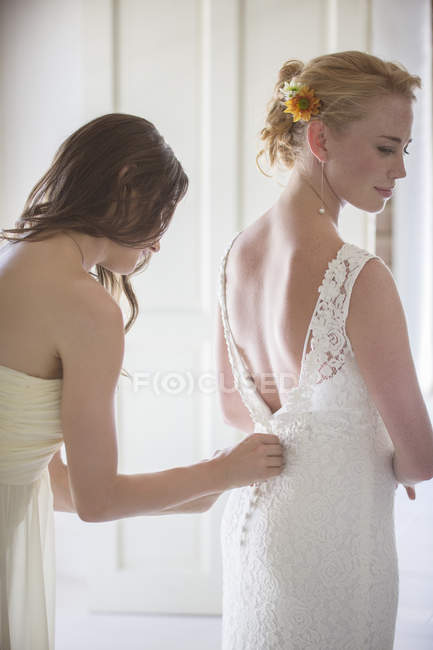 Dama de honra ajudando noiva com vestir no quarto doméstico — Fotografia de Stock