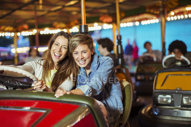 Two cheerful women on bumper car ride in amusement park — Stock Photo