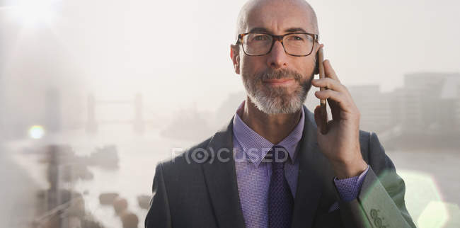 Retrato serio hombre de negocios hablando por teléfono celular en puente urbano, Londres, Reino Unido - foto de stock