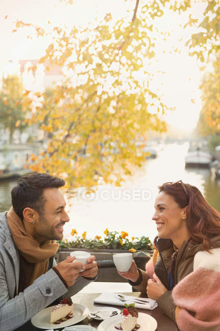Jovem casal beber café e comer sobremesa cheesecake no outono café calçada ao longo do canal — Fotografia de Stock