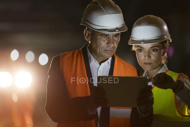 Construction worker and engineer using digital tablet at dark construction site — Stock Photo