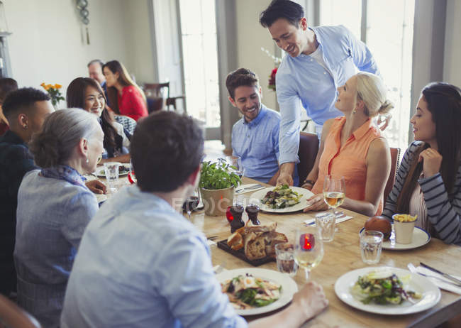 Camarero sirviendo comida a amigos cenando en la mesa del restaurante - foto de stock