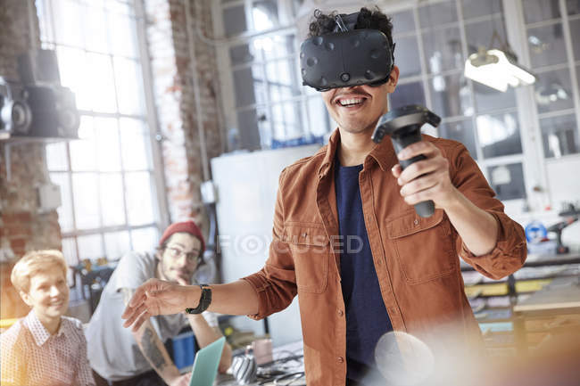 Sourire mâle programmeur d'ordinateur textos réalité virtuelle simulateur lunettes et joystick dans l'atelier — Photo de stock