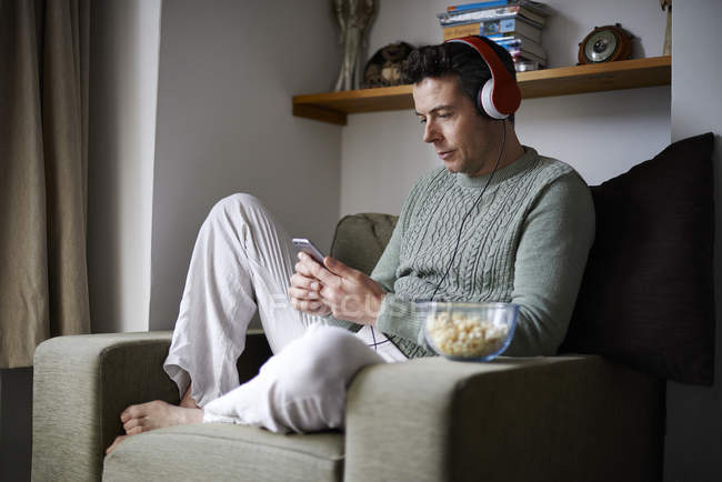 Mann sitzt mit Smartphone im Sessel mit Kopfhörern — Stockfoto