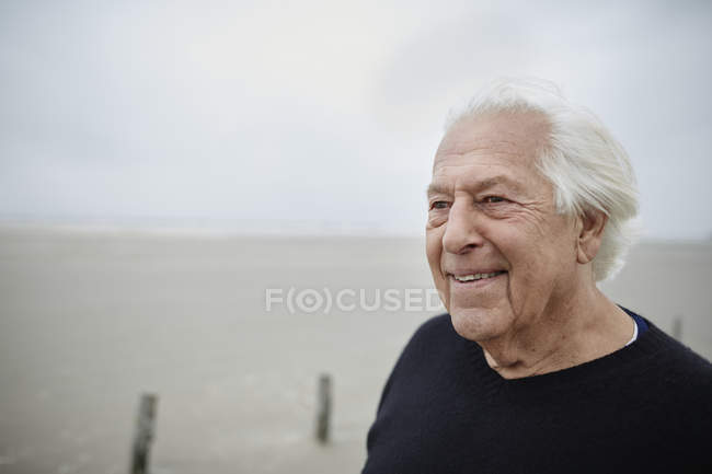 Смолящий вдаль на пляже пожилой мужчина — стоковое фото