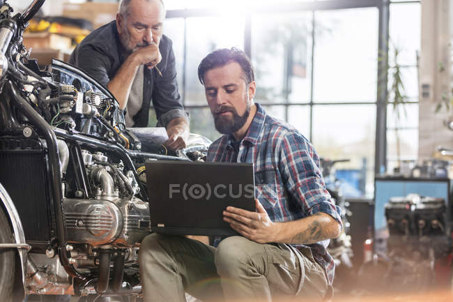 Mecánica masculina de la motocicleta usando el ordenador portátil en taller - foto de stock