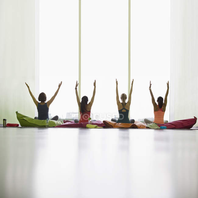 Mujeres en cojines con brazos levantados en estudio de gimnasio de yoga restaurativo - foto de stock
