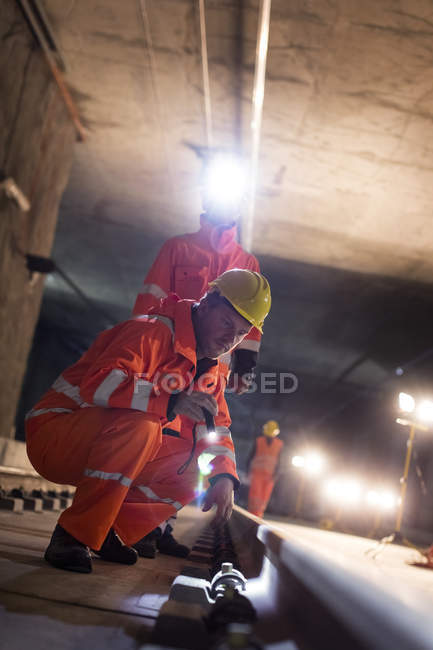Male construction workers examining underground tracks at dark construction site — Stock Photo