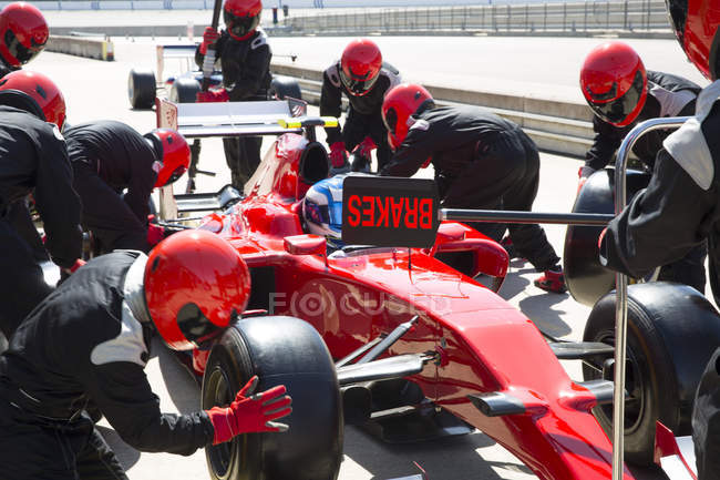 Tripulação do poço substituindo pneus na fórmula um carro de corrida na pista de pit — Fotografia de Stock
