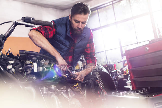Мотомеханик ремонтирует мотоцикл в мастерской — стоковое фото
