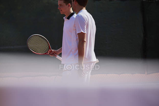 Tenis masculino dobles hablando en pista de tenis soleada - foto de stock