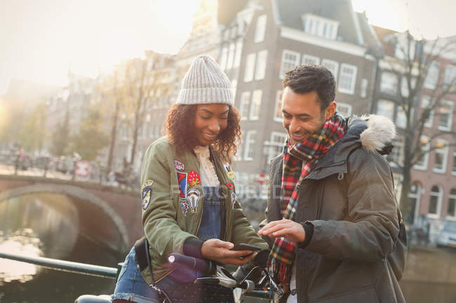Jeune couple avec vélo utilisant un téléphone portable sur un pont urbain, Amsterdam — Photo de stock