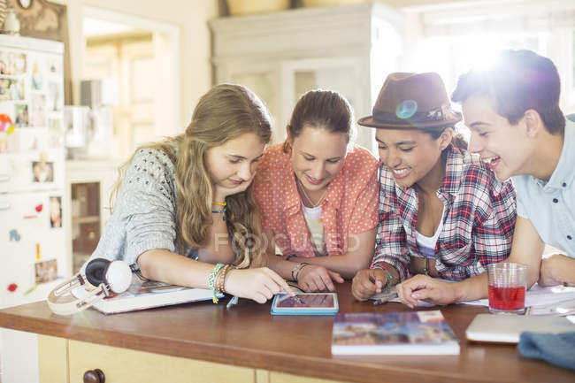 Group of teenagers using together digital tablet at table in kitchen — Stock Photo