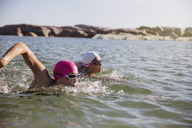 Mulheres nadadoras ativas no oceano contra a costa durante o dia — Fotografia de Stock