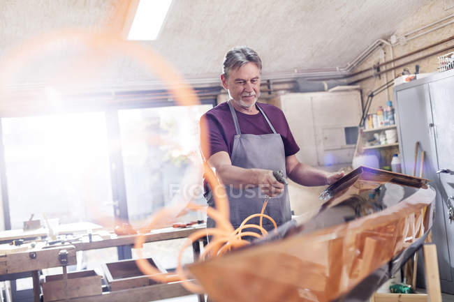Carpinteiro masculino usando compressor de ar, acabamento de caiaque de madeira na oficina — Fotografia de Stock