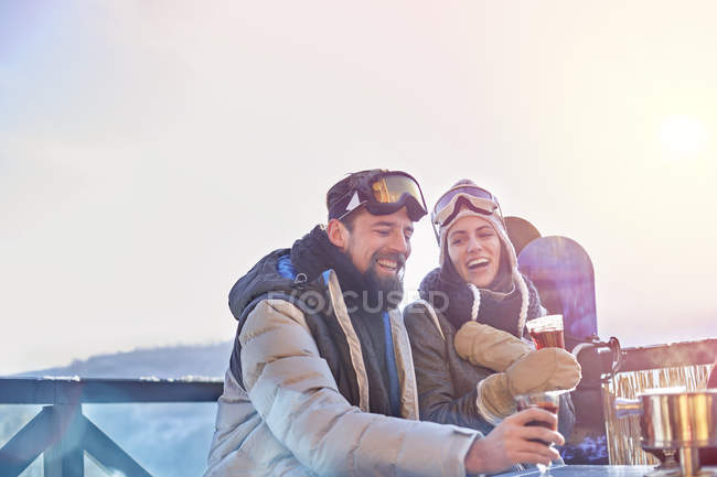 Snowboarder couple laughing, drinking cocktails on sunny balcony apres-ski — Stock Photo