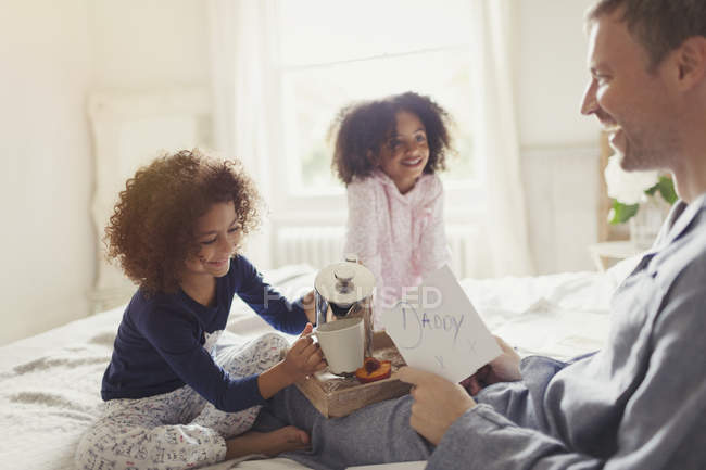 Hijas sirviendo café y tarjeta a padre en la cama en el Día del Padre - foto de stock