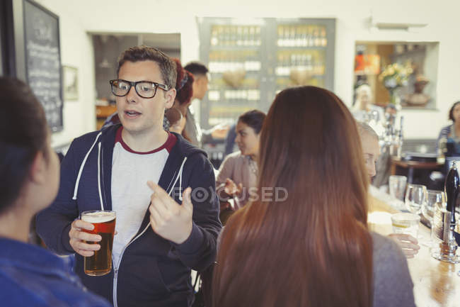 Man drinking beer and talking to woman at bar — Stock Photo
