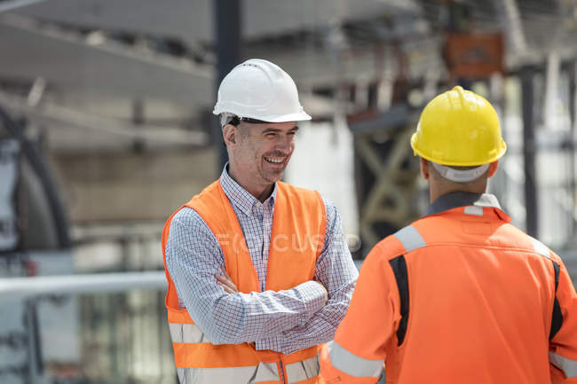 Улыбающийся мастер беседует со строителем на стройке — стоковое фото