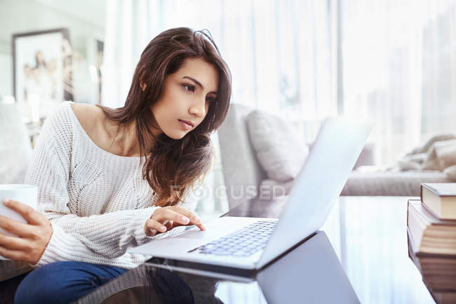 Серйозна жінка використовує ноутбук за обіднім столом — стокове фото
