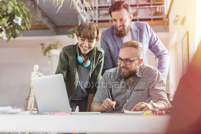 Profesionales del diseño sonrientes usando tabletas gráficas en la computadora portátil en la oficina - foto de stock
