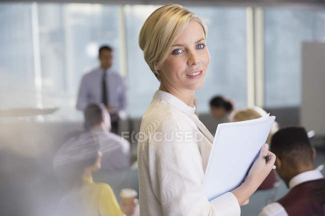 Retrato sonriente mujer de negocios con papeleo en la reunión de la sala de conferencias - foto de stock