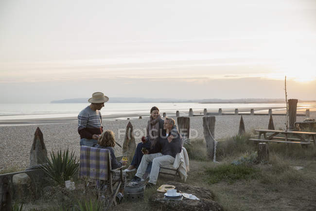 Mature couples barbecuing and drinking wine on sunset beach — Stock Photo