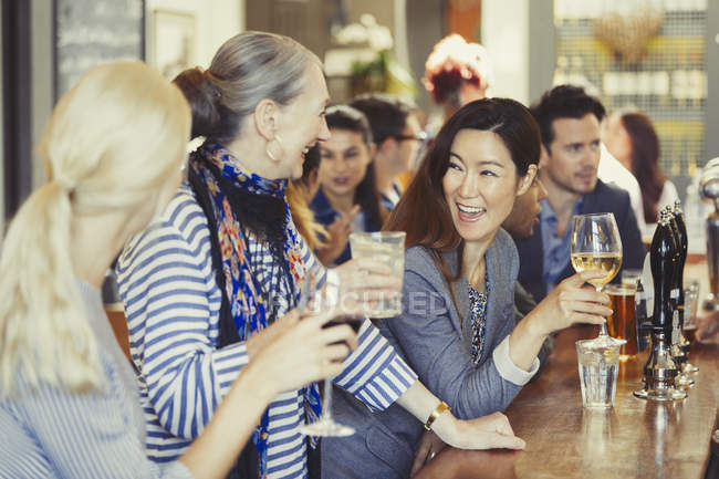 Mujeres sonrientes amigas bebiendo vino en el bar - foto de stock
