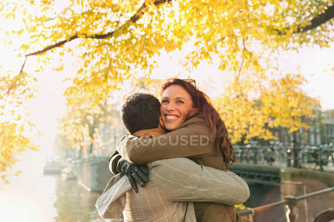 Couple heureux serrant le long du canal d'automne urbain ensoleillé, Amsterdam — Photo de stock