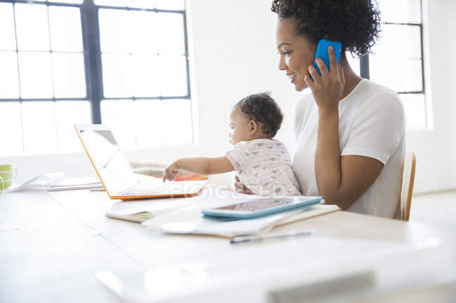 Mother working from home with daughter sitting on her lap — Stock Photo