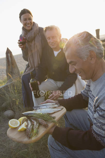 Amigos maduros bebendo vinho e peixe grelhado na praia do pôr-do-sol — Fotografia de Stock