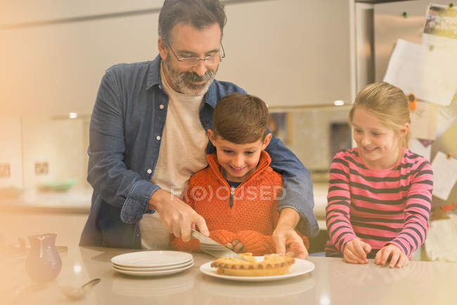 Father cutting and serving pie to children in kitchen — Stock Photo