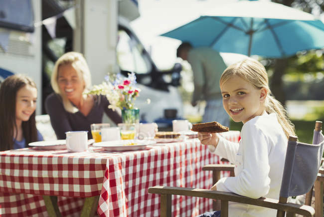 Portrait smiling girl eating breakfast with family outside sunny motor home — Stock Photo