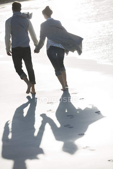 Молодая пара, держась за руки и гуляя по пляжу — стоковое фото