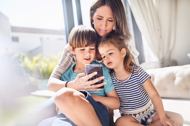 Mãe e crianças usando telefone celular na sala de estar ensolarada — Fotografia de Stock