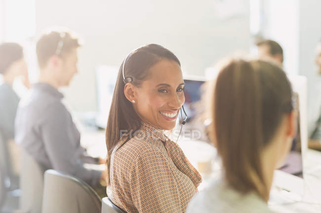 Telemarketers sonrientes con auriculares hablando en una oficina soleada - foto de stock