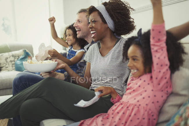 Enthusiastic multi-ethnic young family cheering, watching sports on sofa — Stock Photo