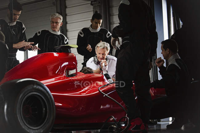 Manager und Boxencrew arbeiten in dunkler Werkstatt an Formel-1-Rennwagen — Stockfoto