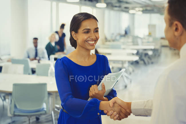 Mujer de negocios sonriente estrechando la mano con un hombre de negocios en el cargo - foto de stock