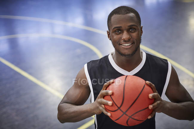 Retrato sorrindo jovem jogador de basquete masculino segurando basquete na quadra — Fotografia de Stock