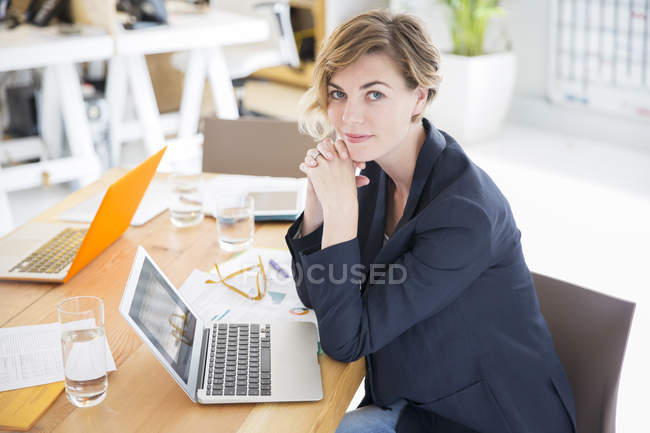 Portrait de femme assise au bureau avec ordinateur portable au bureau — Photo de stock