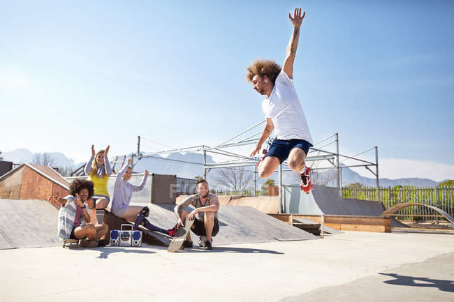 Friends watching and cheering man jumping in roller skates at sunny skate park — Stock Photo
